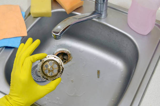 Detergente in guanti di gomma mostra i rifiuti nel protettore dello scarico di un lavello da cucina
 - Foto, immagini