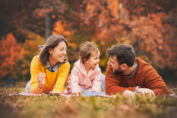 Enjoying every moment together. Happy young family of three smiling while lying on grass in park - Foto, imagen