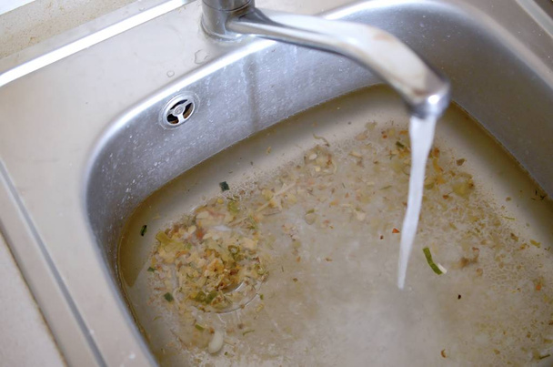 Rozsdamentes acél mosogató dugó lyuk közelről tele a víz és az élelmiszer-részecskék - Fotó, kép