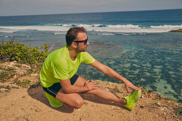 Sportsman stretching on a tropical exotic cliff near the ocean. - Valokuva, kuva