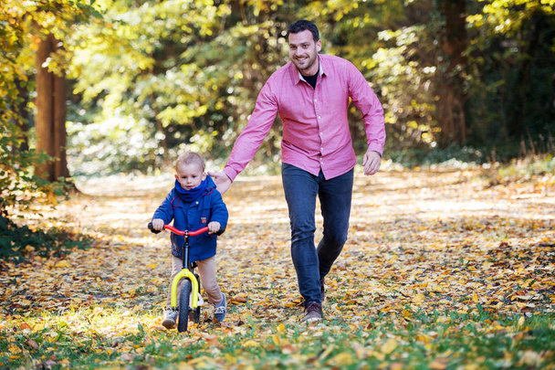 Father and small son with a balance bike on a walk in autumn forest. - Fotoğraf, Görsel