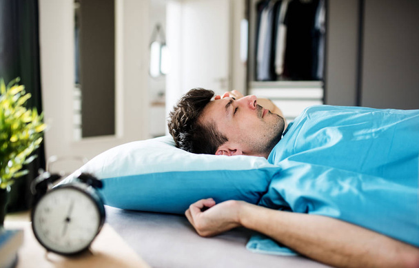Young man with alarm clock in bed at home, sleeping. - Foto, Bild