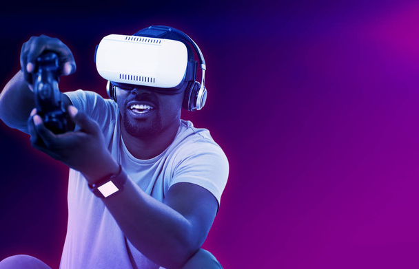 Mann mit Virtual-Reality-Headset und Videospiel vor türkisfarbenem und violettem Hintergrund - Foto, Bild