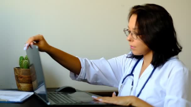 Bliska nieznanych kobiet lekarz siedzi przy stole w szpitalu i wpisując na komputerze przenośnym. Młoda kobieta Doktor pielęgniarka w biurze kliniki szpitalnej. - Materiał filmowy, wideo