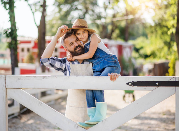 A portrait of father with small daughter outdoors on family farm. - Foto, Imagen