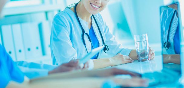 Médico sonriente usando un portátil trabajando con sus colegas en una habitación de hospital luminosa - Foto, Imagen