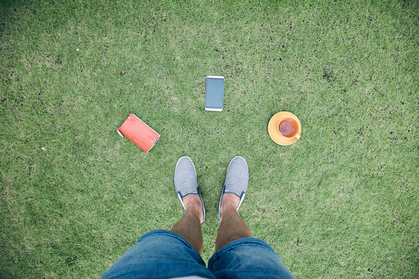 Homem com smartphone, xícara de café / chá e notebook em uma grama
 - Foto, Imagem