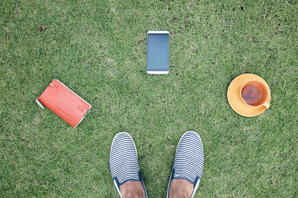 Férfi okostelefon, csésze od kávé/tea és notebook a fűben - Fotó, kép