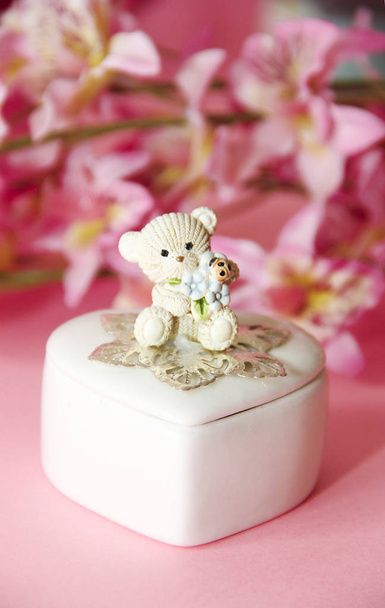 ceramic white casket with a teddy bear on a background of pink flowers and hearts - Photo, Image