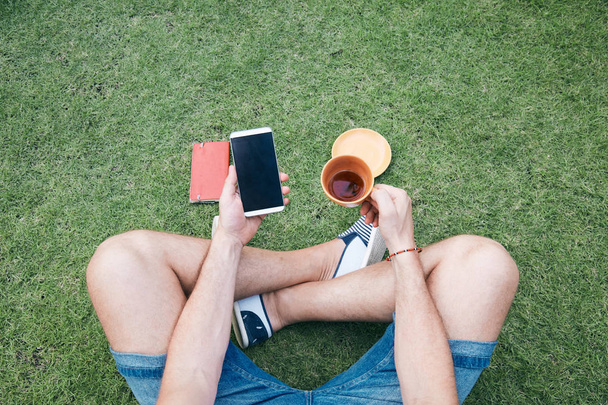 Uomo che usa smartphone e beve caffè / tè su un'erba
. - Foto, immagini
