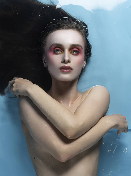 A beautiful naked girl with conceptual makeup in red tones is la - Φωτογραφία, εικόνα
