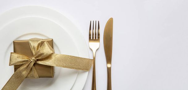 Διαμόρφωση τραπεζιού, Χριστούγεννα, Πρωτοχρονιά. Χρυσά μαχαιροπίρουνα σε λευκό σετ πιάτων, λευκό φόντο - Φωτογραφία, εικόνα