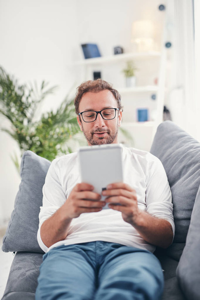 Mann nutzt Tablet und surft im Wohnzimmer im Internet. - Foto, Bild