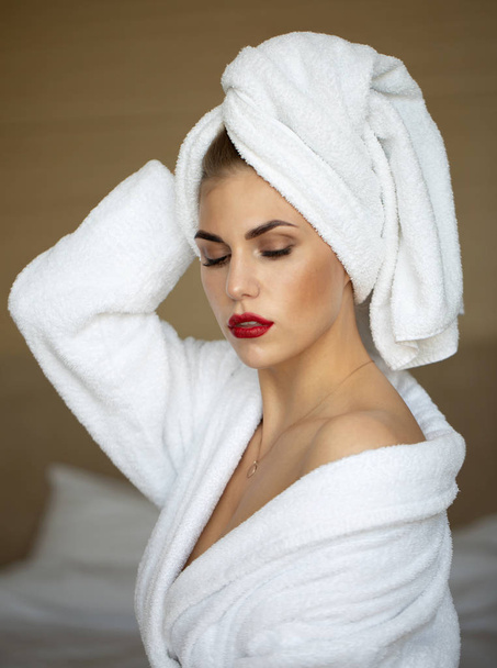 Portrait of blonde woman with bright makeup in bathrobe posing in hotel room - Photo, image