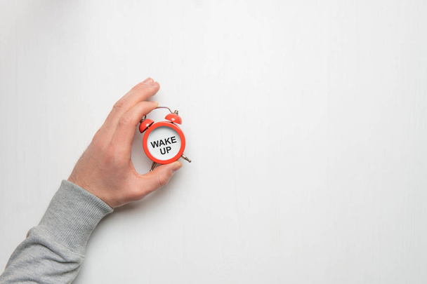 La mano de un joven sostiene un despertador rojo. Tiempo, sueño, aw
 - Foto, imagen