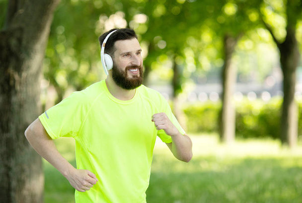 Hombre barbudo joven en auriculares y entrenamiento de ropa deportiva en el parque
 - Foto, imagen