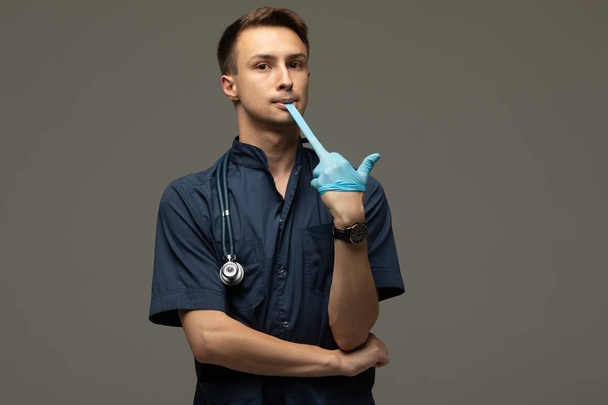 Young male doctor putting on medical gloves preparing for examination smiling to the camera cheerfully, confidence, medicine and healthcare occupation concept - 写真・画像