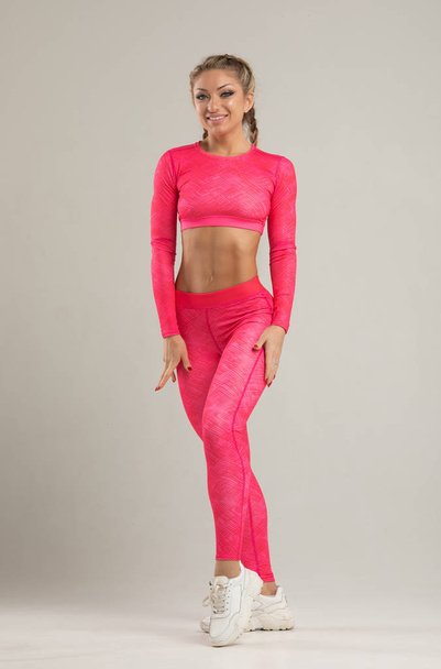 Young blonde fit woman in bright pink sportswear posing in studio - Фото, изображение