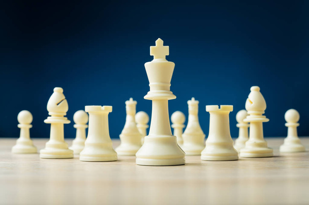 White chess pieces with king in front placed on wooden desk - Foto, afbeelding