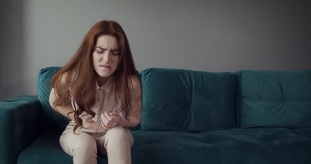 Redhead woman sits on the couch and feels belly pain and anger. - Felvétel, videó