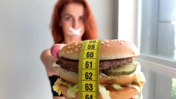 Dieta. Retrato de una mujer quiere comer una hamburguesa, pero una boca pegada, una noción de dieta, comida poco saludable, una voluntad en la nutrición
. - Metraje, vídeo
