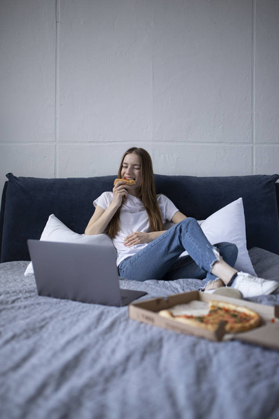 Happy young woman eating slice of hot pizza at home and watching - Foto, immagini