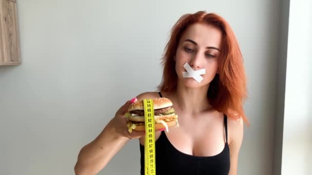Dieta. Retrato de una mujer quiere comer una hamburguesa, pero una boca pegada, una noción de dieta, comida poco saludable, una voluntad en la nutrición
. - Metraje, vídeo