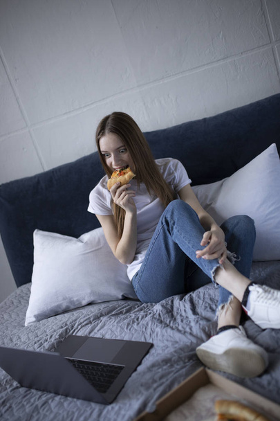 Gelukkig jonge vrouw eten slice van hete pizza thuis en kijken - Foto, afbeelding