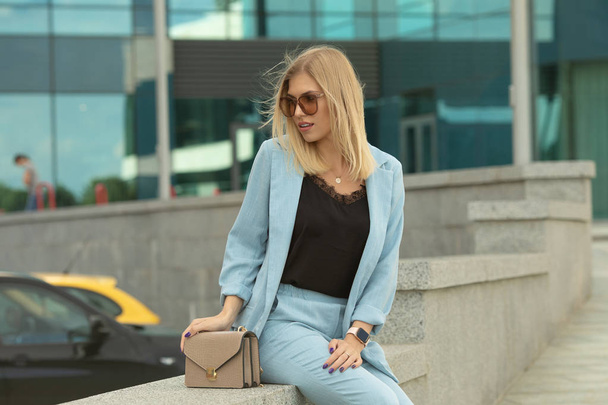 Elegant blonde woman in blue suit and sunglasses posing on urban background - Zdjęcie, obraz