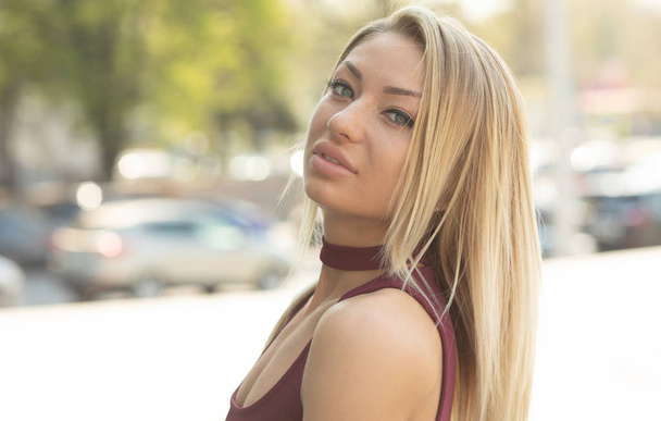 Portrait of young blonde woman in burgundy dress posing on urban background - 写真・画像