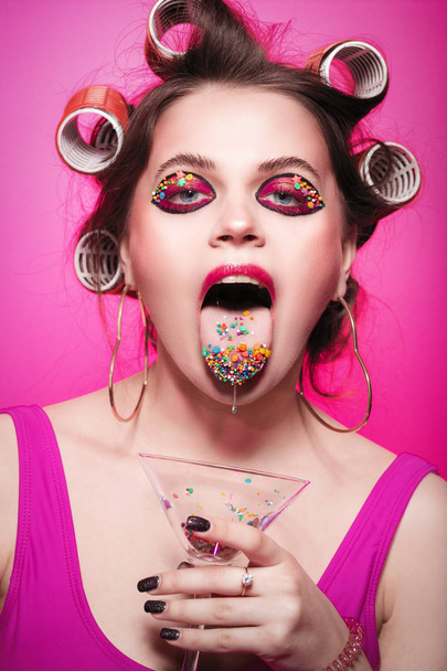 キャンディーのポーズを持つ舌とガラスにお菓子を持つ生意気な女の子  - 写真・画像