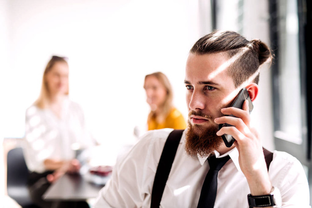 A portrait of young businessman with smartphone in an office, making call. - Foto, Imagen