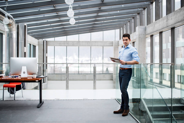 A portrait of young businessman standing indoors in an office. - Foto, immagini