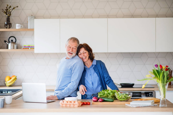 A portrait of senior couple with laptop indoors at home, cooking. - Foto, afbeelding