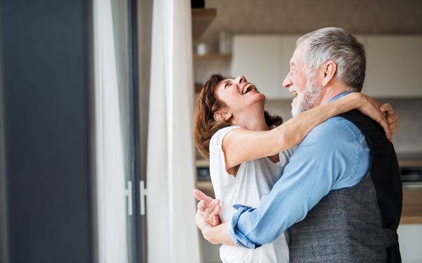 A senior couple indoors at home, laughing and hugging. - Photo, image