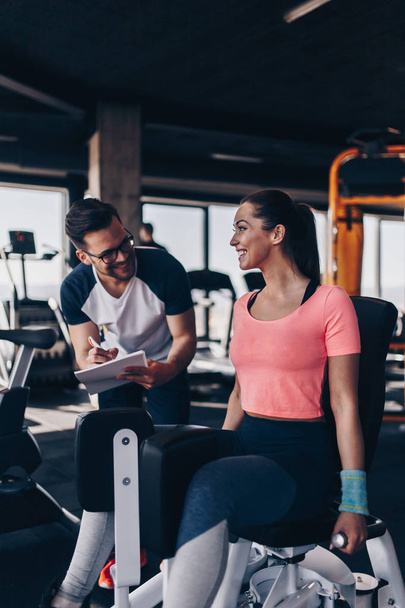Jeune femme en forme et séduisante travaillant dans une salle de gym moderne avec son instructeur de fitness personnel ou son entraîneur. - Photo, image