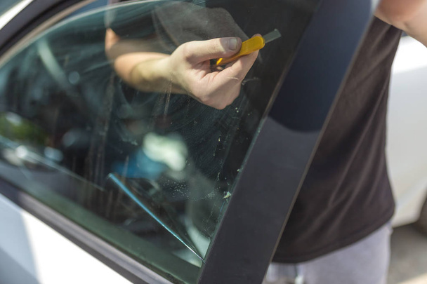 Worker removing old car window glass protective tint foil from side window. - Foto, afbeelding