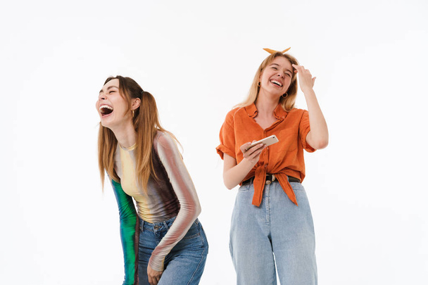 Photo of two happy girls wearing colorful clothes laughing while holding smartphones together - Foto, Imagem