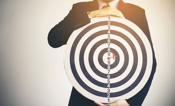 Businessman holding dartboard with a darts aiming at the target, - Foto, imagen