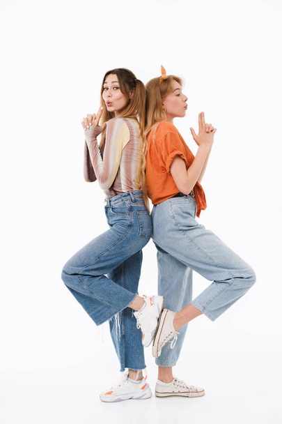 Photo of two cool girls wearing colorful clothes standing back to back and doing gun gesture with fingers - Zdjęcie, obraz