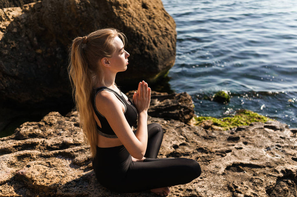 Beautiful calm young girl meditating while sitting at the beach - Foto, Bild