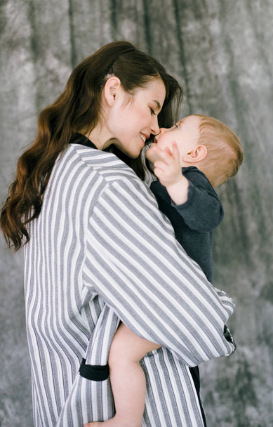 Young beautiful mother in a fashionable pantsuit holds the baby in her arms in a bright studio - Fotoğraf, Görsel