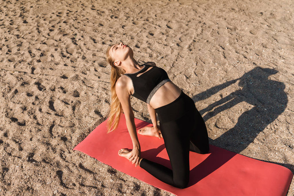 Image of concentrated strong woman doing yoga exercises on mat at seaside in morning - Fotografie, Obrázek