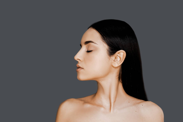 Beauty concept, skin care, hair care and healsy skin. Brunet woman showing her perfect skin on face after cosmetology procedure, clean her face over grey studio background and copy space.  - Valokuva, kuva