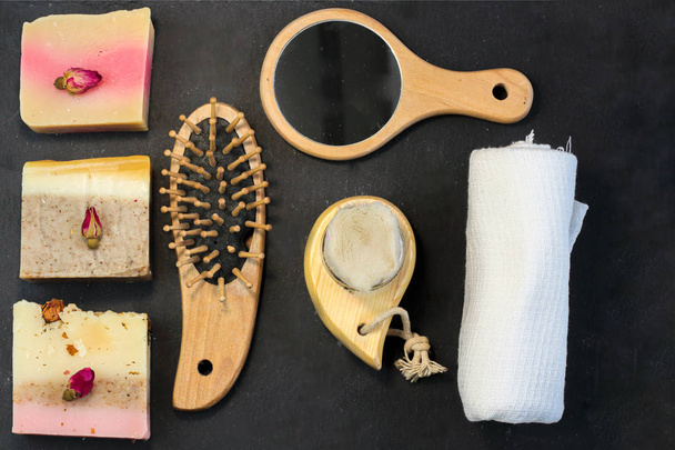 Χειροποίητο πολύχρωμο σαπούνι με βότανα και μπουμπούκια, χτένα, πετσέτα, καθρέφτη, πινέλο προσώπου σε μαύρο φόντο με. Κιτ σετ Spa για θεραπείες προσώπου και σώματος επίπεδη στυλ - Φωτογραφία, εικόνα