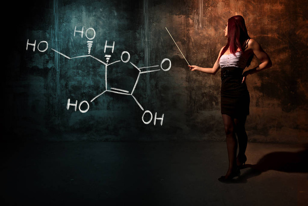 Sexy meisje of secretaresse of vrouwelijke student presenteren hand getekende chemische formule van vitamine C - Foto, afbeelding