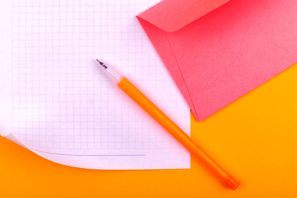 A fehér papírlapot a rajzok, szövegek, levelek és jegyzetek mellett egy sárga tollat és egy rózsaszín borítékot a betűk fekszik narancssárga háttér - Fotó, kép