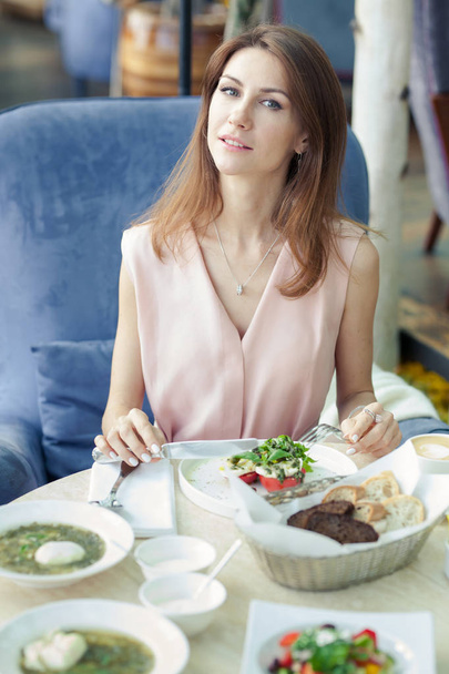 Portrait of beautiful young woman in a pink dress has lunch in a restaurant. Food and drinks on the table. - Foto, imagen