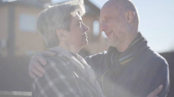 Porträt eines erwachsenen Ehepaares, das im kühlen, windigen, sonnigen Wetter vor dem Hintergrund seines Hauses steht. - Filmmaterial, Video