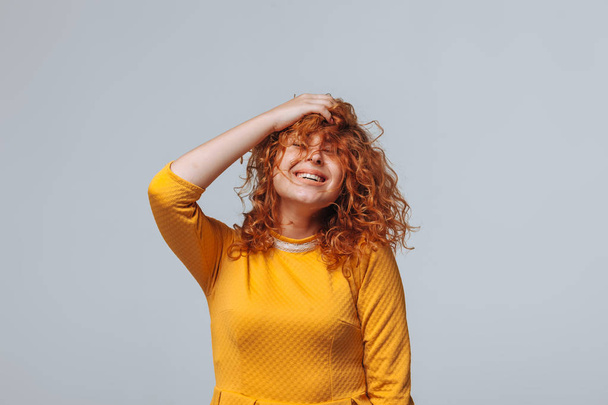 Red curly girl in a yellow dress on a light gray background smil - Photo, Image